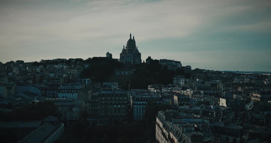 The iconic Sacré-Cœur Basilica sits atop Montmartre hill overlooking the moody, silhouetted Paris skyline at dusk