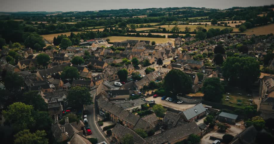 Slow aerial pan reveals a charming historic village nestled in the lush green English countryside