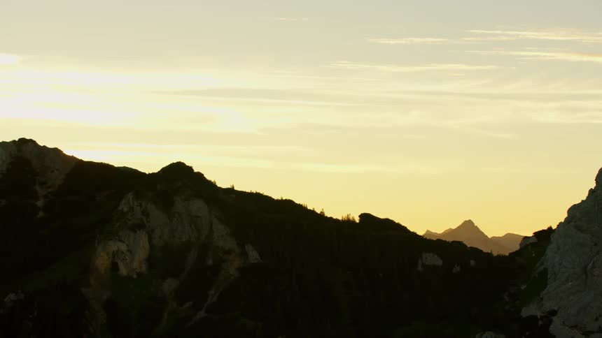 The sun rises above tall mountain peaks