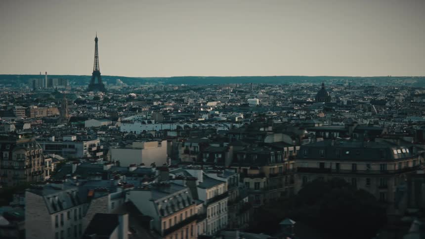 A cinematic aerial shot slowly pans right across the rooftops of Paris, showcasing the iconic Eiffel Tower against the evening sky