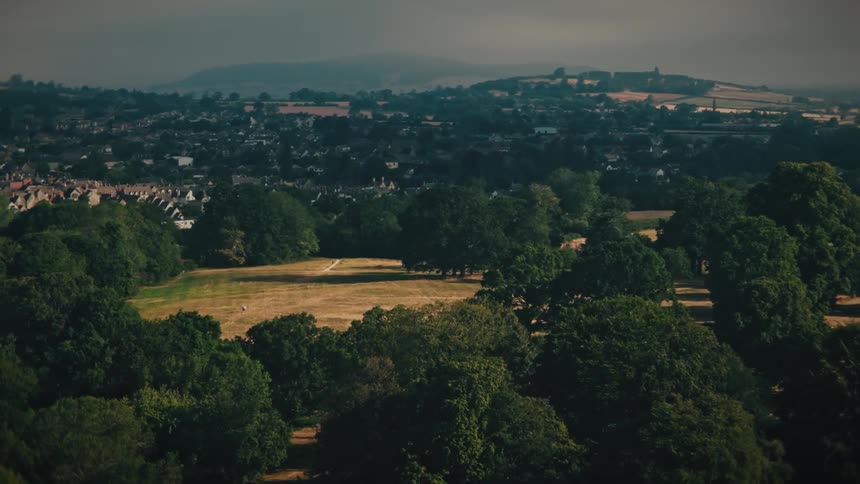 Slowly panning aerial shot of a large park and town nestled in the English countryside on a cloudy day