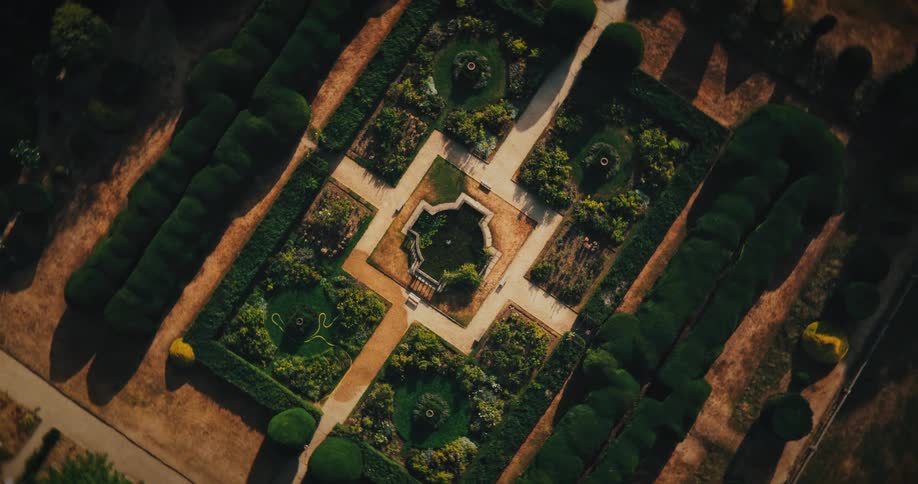A slow, top-down aerial zoom-out reveals an elegant and symmetrical formal garden with a central fountain and manicured hedges