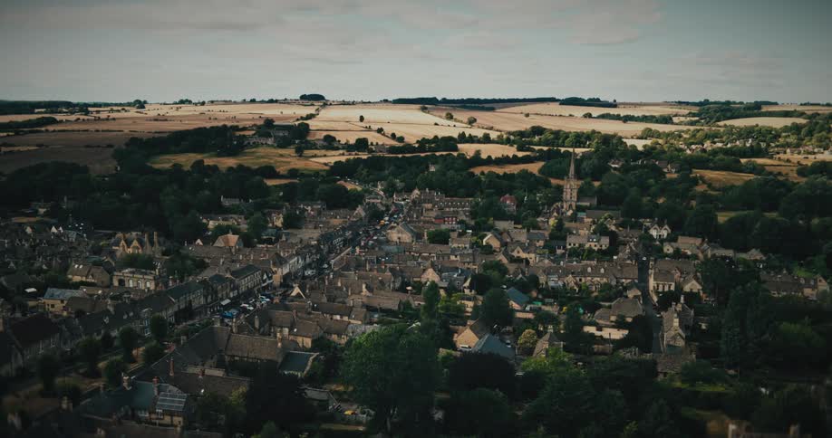 A moody aerial shot of a historic English village nestled in the green rolling countryside under a cloudy sky