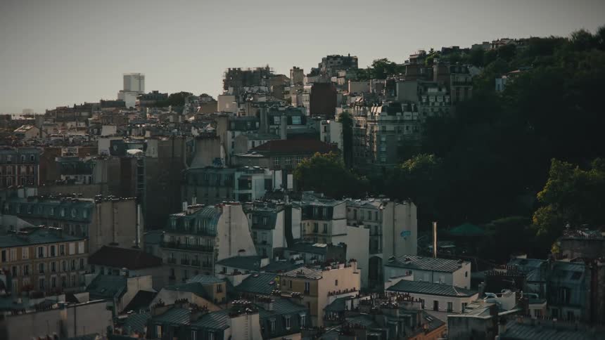 A cinematic aerial view slowly pushes in over the dense historic rooftops of a Parisian neighborhood during a hazy sunset