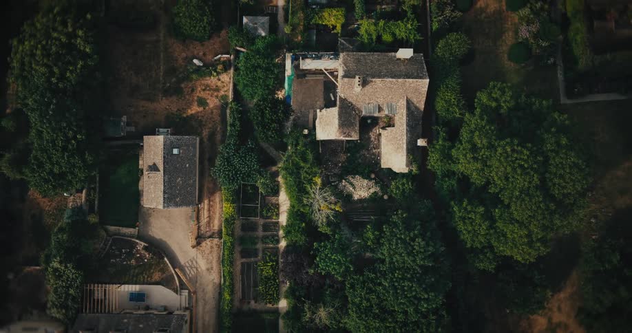 A slow aerial top-down reveal of a charming stone house undergoing renovation, surrounded by lush green trees and gardens in a quiet neighborhood
