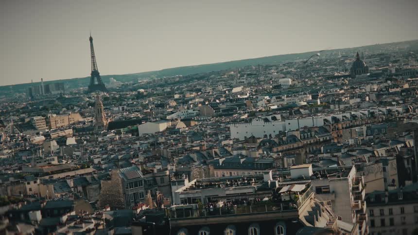 A dramatic Dutch-angle high shot of Paris slowly pulls back and levels to reveal the iconic Eiffel Tower and sprawling city skyline