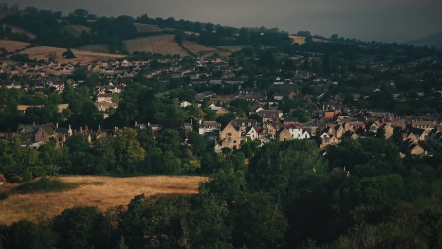 A slow cinematic reveal of a picturesque English town nestled in a valley surrounded by lush green countryside