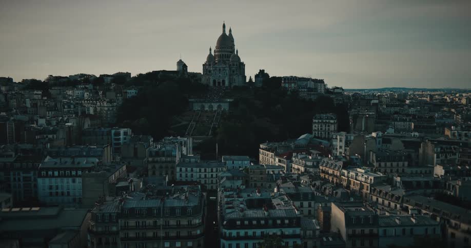 A wide, static shot of the Sacré-Cœur Basilica on Montmartre hill overlooking the rooftops of Paris as evening falls