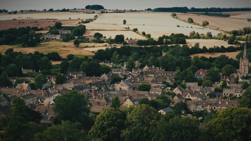 An aerial view of a picturesque old town nestled in the lush green countryside, with the camera slowly pulling back