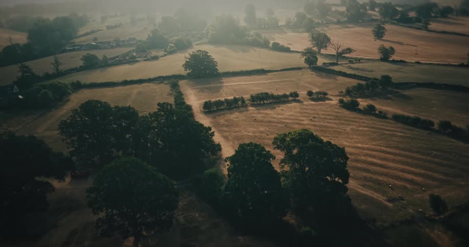 An aerial view flies over the atmospheric ruins of an old manor and its formal gardens, revealing the vast, misty English countryside at sunrise