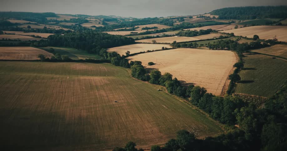 A serene aerial flight over a vast rural landscape of patchwork fields and rolling hills