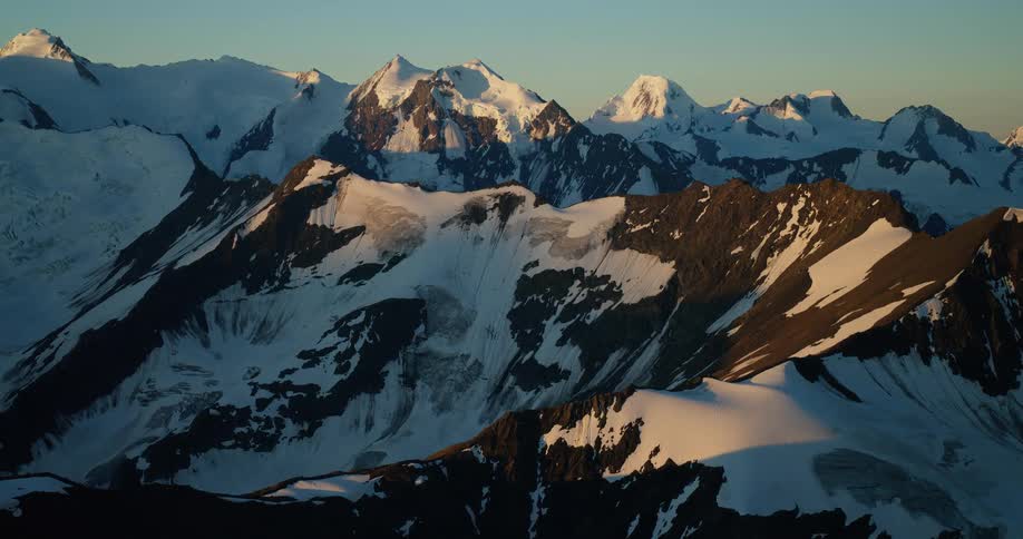 A stunning static view of a vast, snow-covered mountain range bathed in the warm, golden light of sunrise
