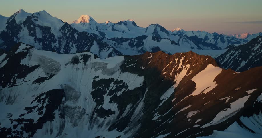 An epic, slow zoom-in reveals a vast, snowy mountain range with glaciers, bathed in the soft, warm glow of sunrise