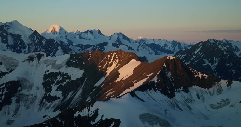 A majestic static shot of a vast, snow-covered mountain range illuminated by the warm light of sunrise