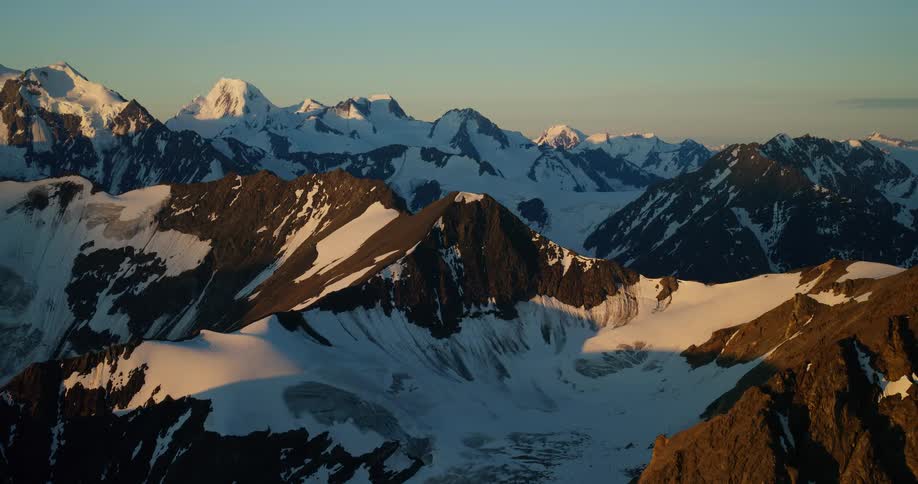 A majestic snow-capped mountain range is bathed in the warm, golden light of sunrise