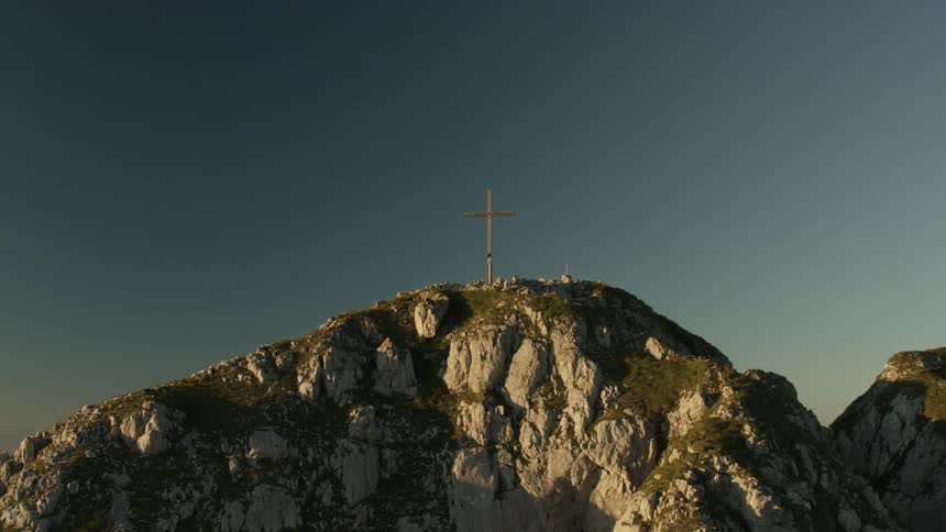 Large cross sitting high above on a mountaintop near sunset