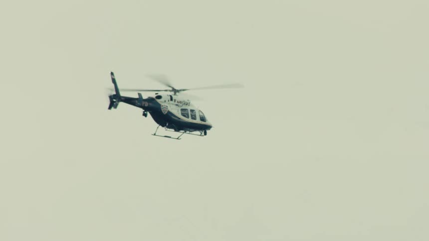 An NYPD police helicopter hovers in the air against a bright, overcast sky while on patrol