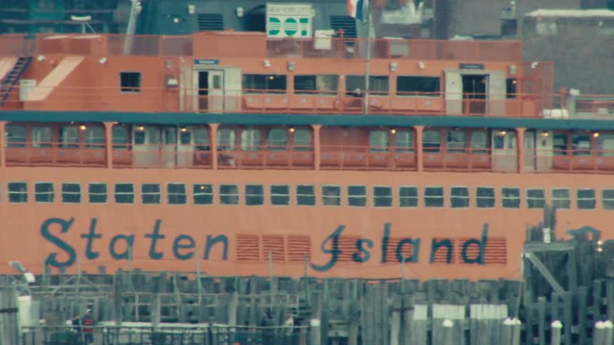 A slow-panning, close-up shot of the iconic orange Staten Island Ferry in New York City