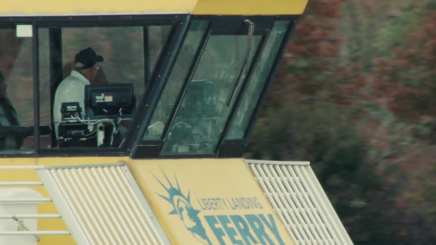 A telephoto shot captures the captain in the pilot house steering the yellow Liberty Landing Ferry