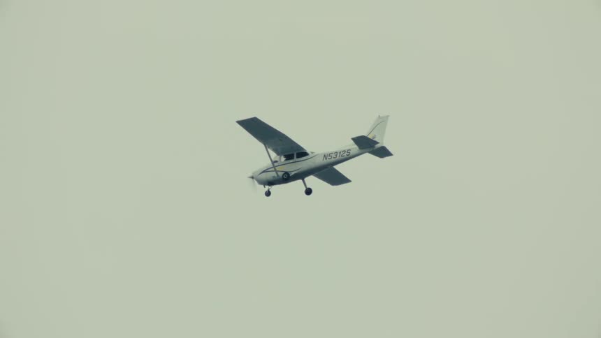 A small, single-propeller airplane glides in slow motion across a vast, overcast sky