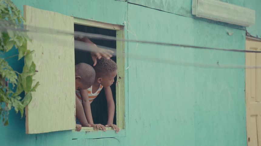 Two curious young boys peer out of an open window of their turquoise home while an adult points something out to them