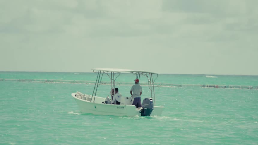 A small motorboat with a canopy carrying two men idles in the beautiful turquoise waters of the ocean