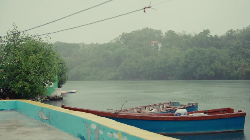 Colorful fishing boats are docked on a tranquil river during a heavy downpour