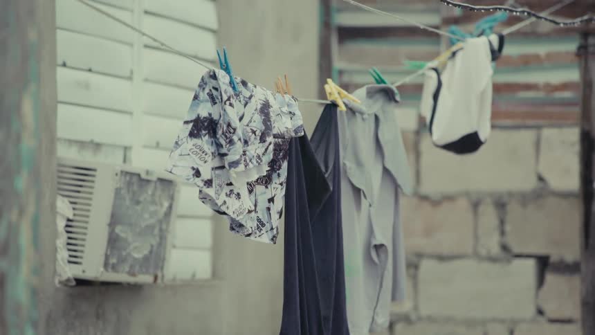 A light rain falls on freshly washed laundry hanging on a clothesline in an urban backyard