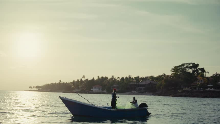 Two fishermen on a small motorboat pull in their nets from the ocean at sunset