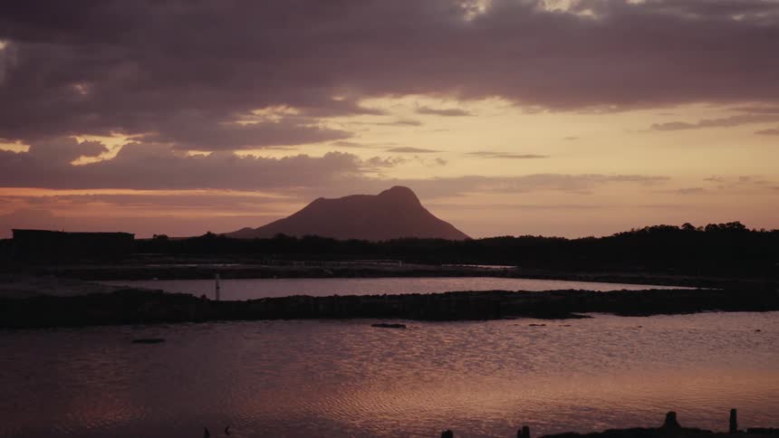 A tranquil lake reflects the beautiful colors of a sunset sky behind a silhouetted mountain