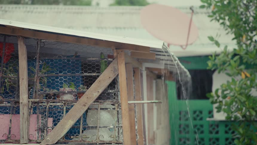 Heavy rain pours from the tin roof of a simple, rustic home in a developing country during a storm