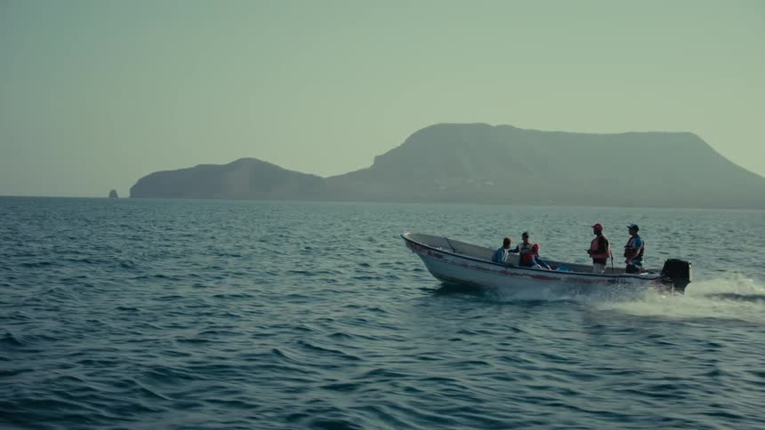 Slow motion shot of a passenger boat cruising across the ocean with a hazy, mountainous island in the distance