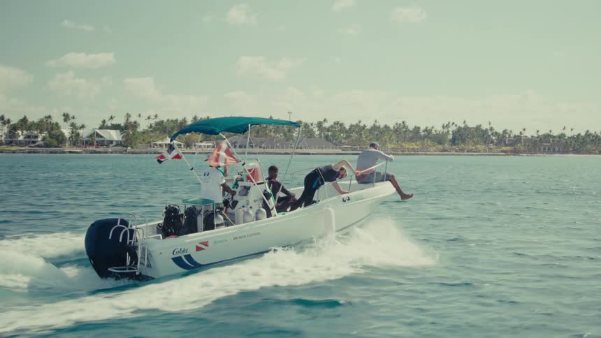 Slow-motion side view of a dive boat carrying scuba divers as it speeds across the ocean along a tropical coastline