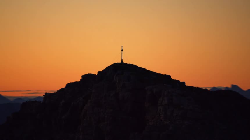 A cross stands on a mountain peak at sunset