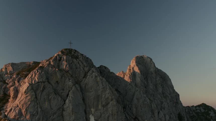 A cross is perched atop a high mountain peak