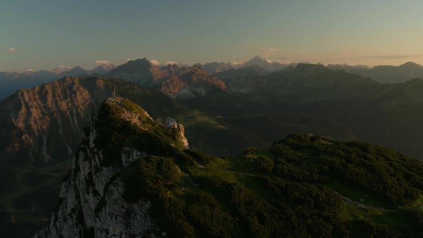 Large cross sitting high above on a mountaintop near sunset