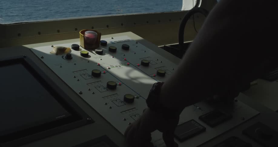 A sailor's hands adjust the knobs and buttons on a ship's control panel while sailing on the ocean