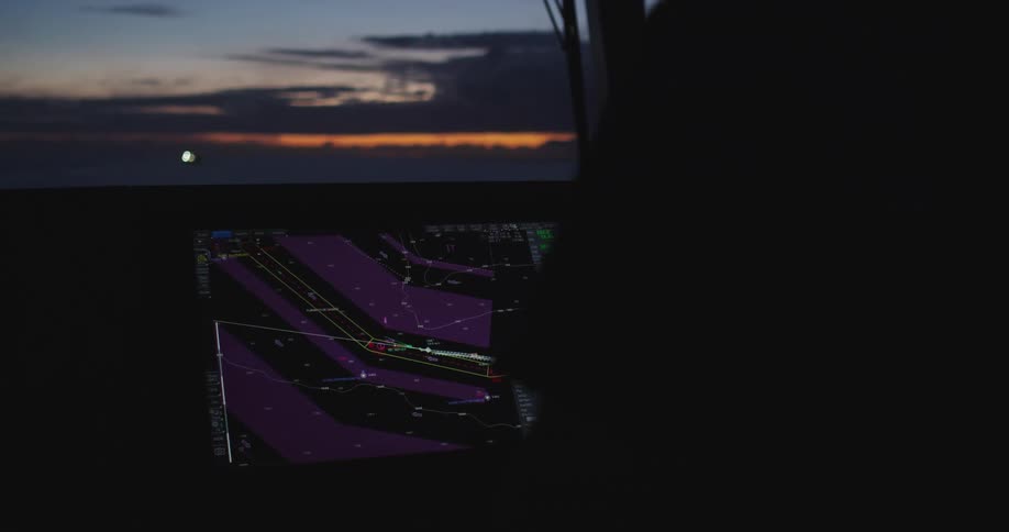 Electronic navigation screens glow on a ship's bridge as it sails through the ocean at dusk