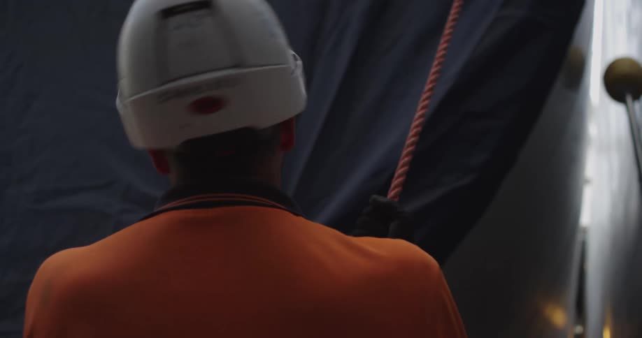 Over-the-shoulder shot of an industrial worker wearing a hard hat and holding a rope