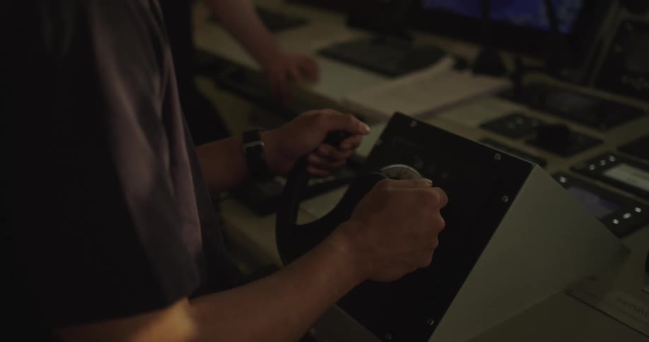 A close-up of a ship captain's hands steering the vessel from the helm in the dimly lit control room