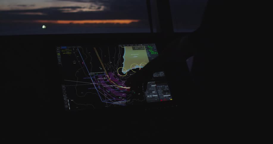 A ship's navigator uses a sophisticated touchscreen chart plotter on the bridge at dusk to plan a route