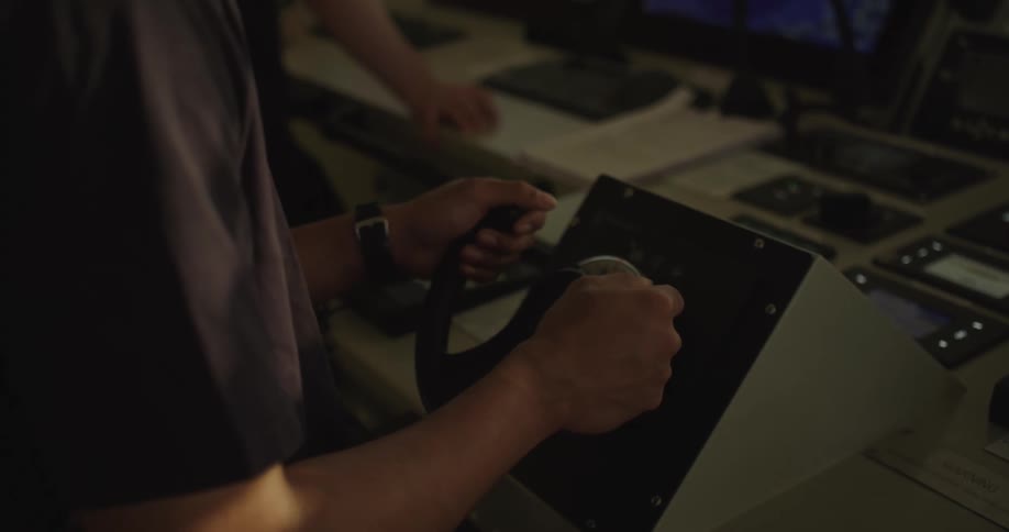 A ship's captain navigates the vessel from the dimly lit control room, his hands firmly on the steering wheel