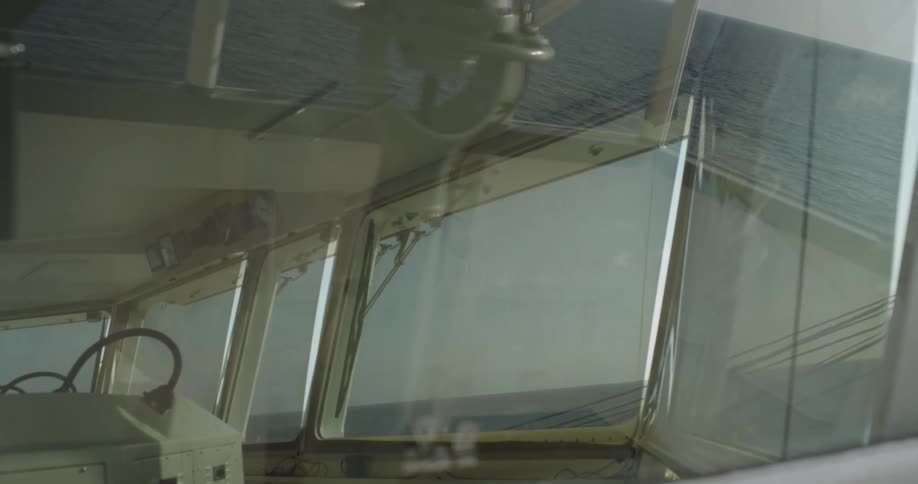 A calm view of the open ocean as seen through the reflective windshield of a moving ship's bridge