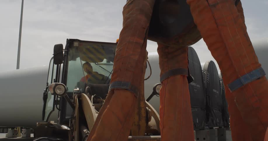 A low-angle view of a large industrial crane hook and straps preparing to lift a massive wind turbine blade at a construction site