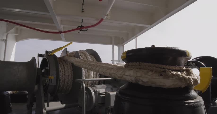 A mooring winch with thick rope is secured on the deck of a ship during the day