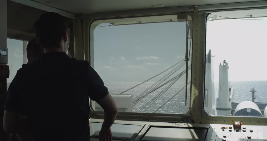 A sailor gives hand signals while looking out at the open ocean from the bridge of a large cargo ship