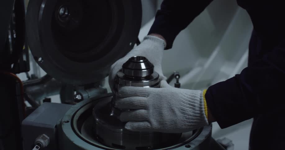 An engineer wearing protective gloves carefully assembles a complex piece of industrial machinery