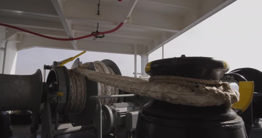 A close-up view of a large mooring winch with a thick rope slowly turning on the deck of a ship