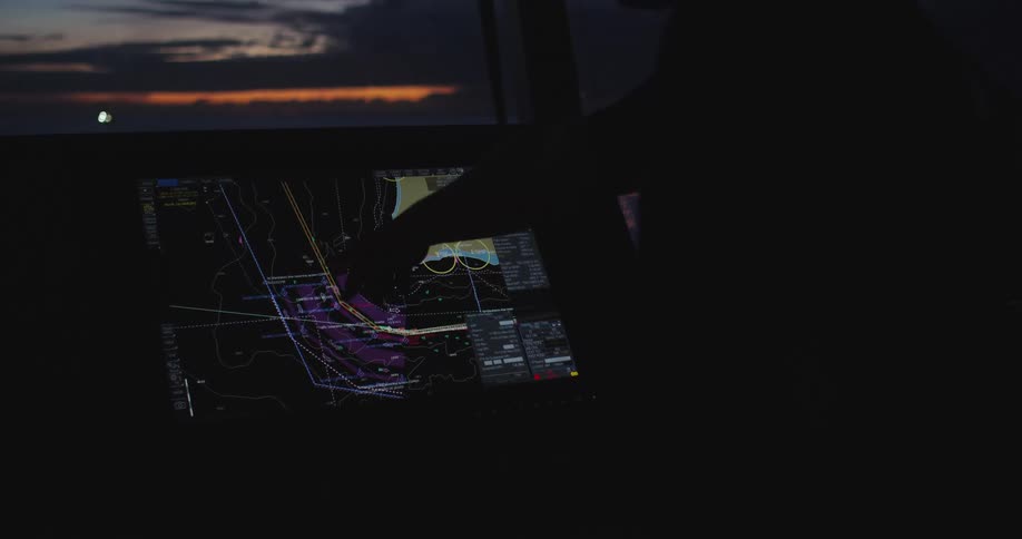 A silhouetted captain on a ship's bridge uses a digital touchscreen map to navigate at sunset