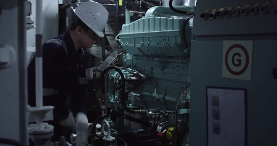 An engineer wearing a hard hat and protective gloves diligently performs maintenance on a large industrial Cummins engine